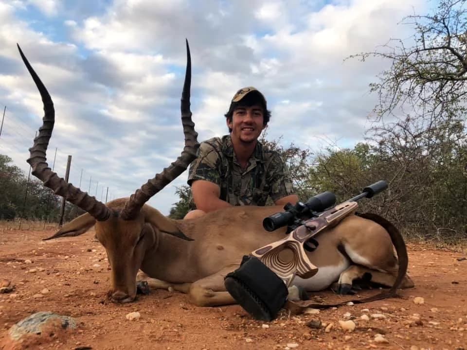 A hunter with an impala ram, rifle on a bipod