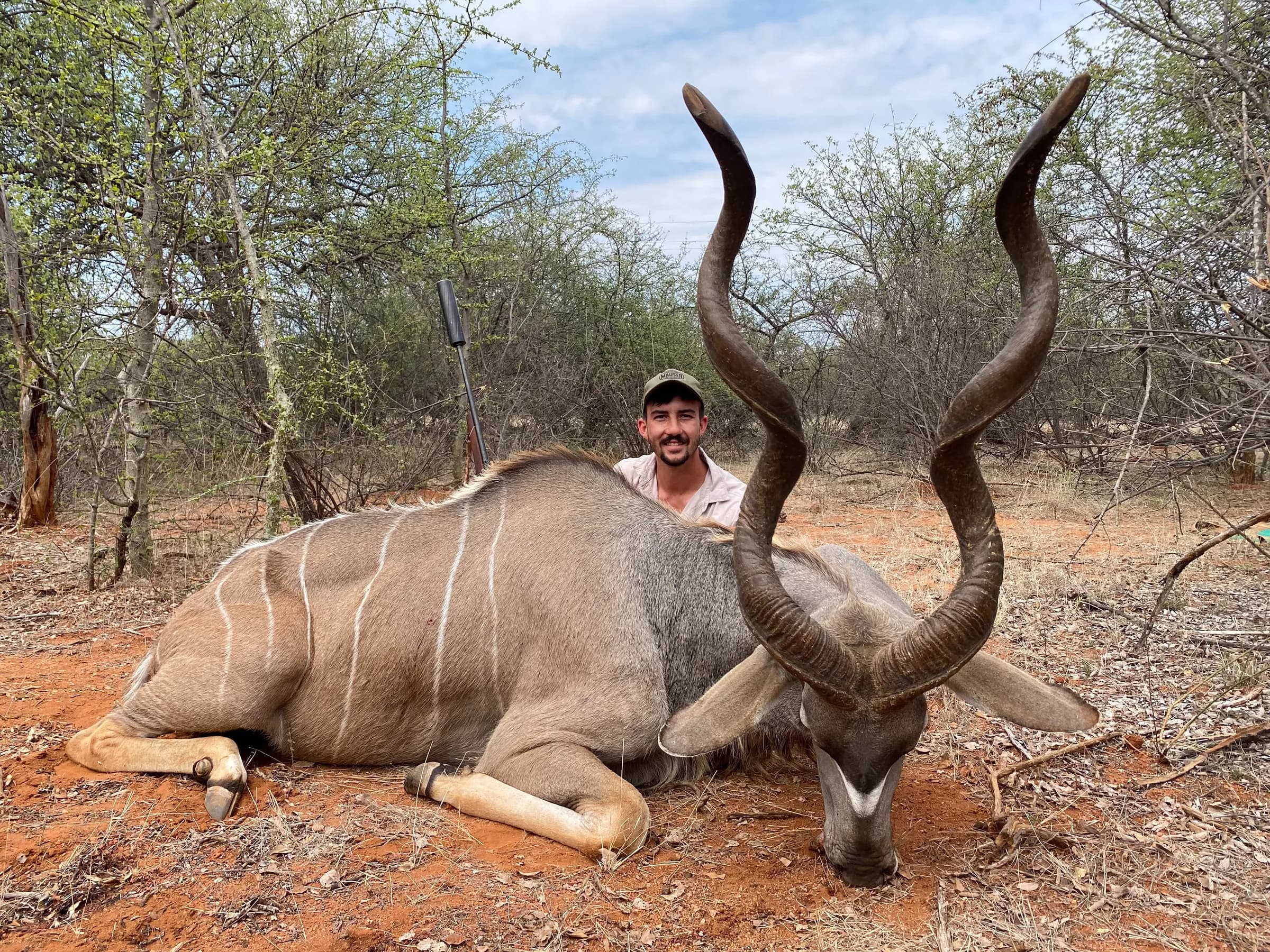 A hunter with a heavy-horned kudu bull on red soil