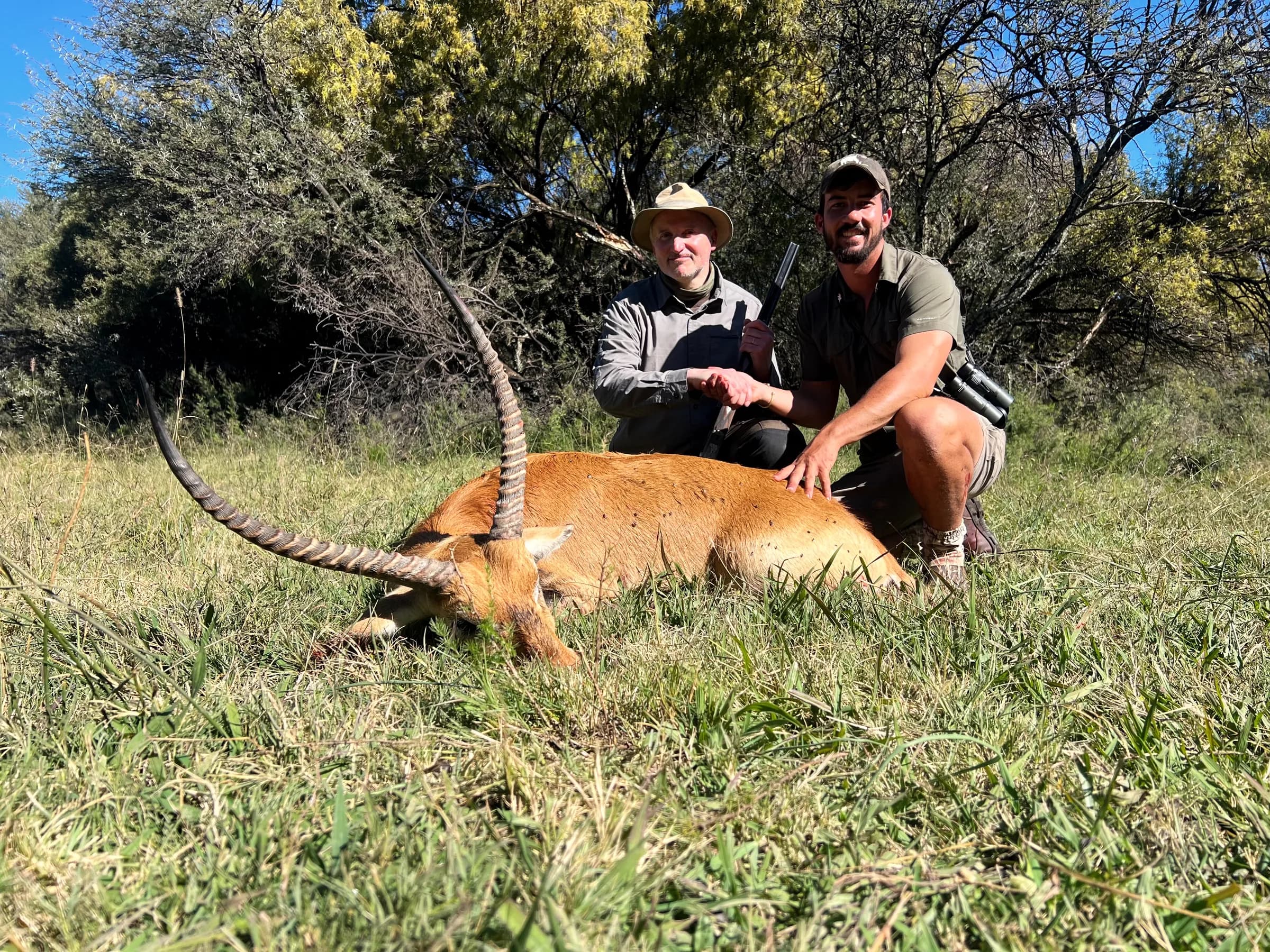 Two hunters with a plains-game trophy in long grass
