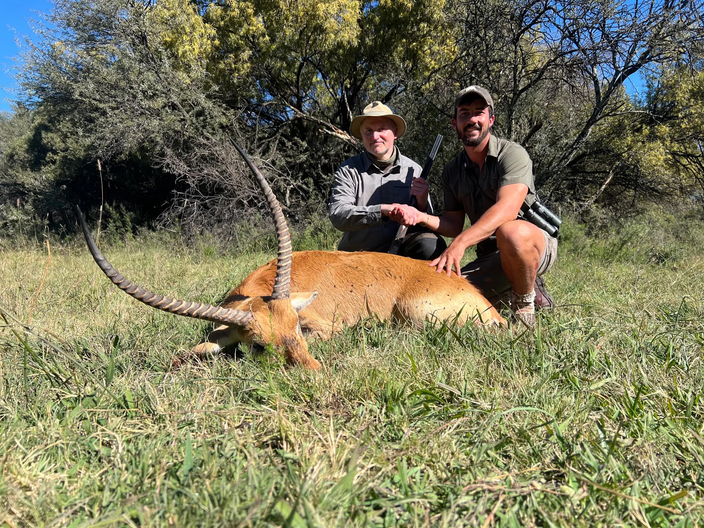 Two hunters with a plains-game trophy in long grass